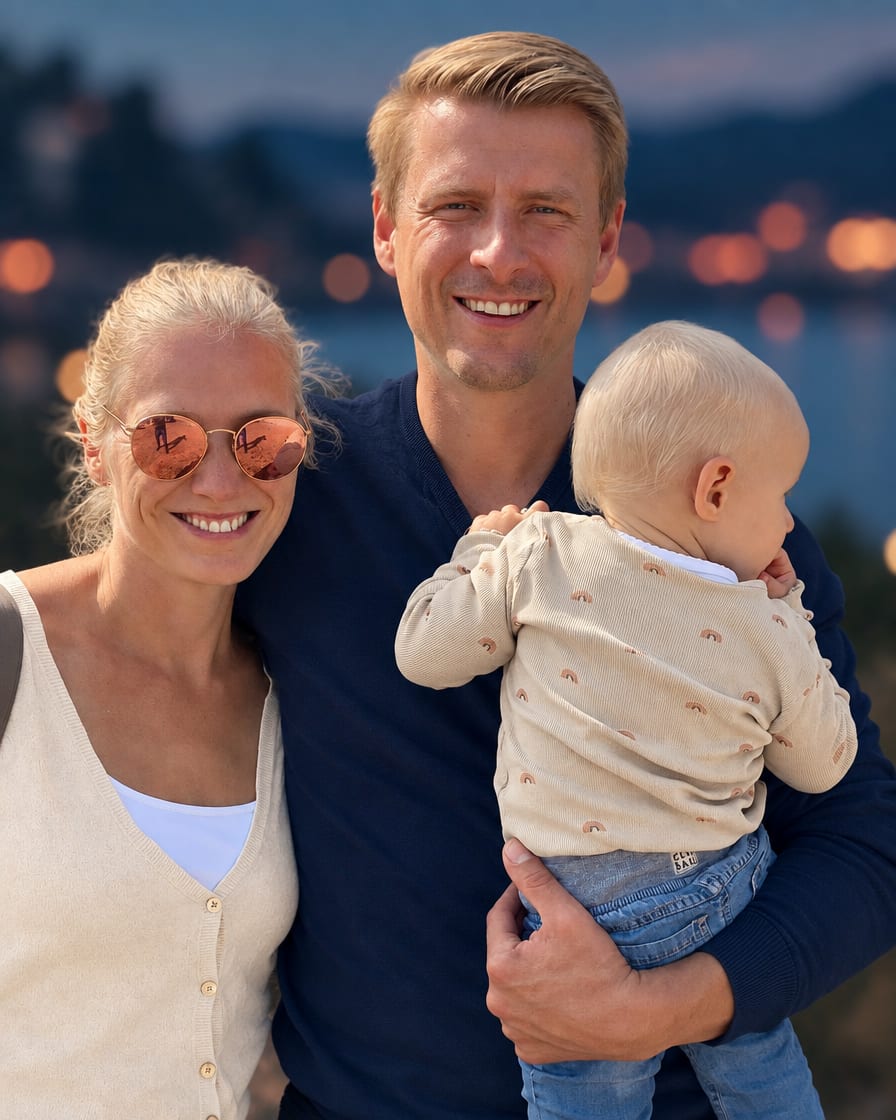 Michael Scholz lächelt in die Kamera, im Arm ein Kleinkind; neben ihm seine Frau mit Sonnenbrille, dahinter der Abendhimmel am See